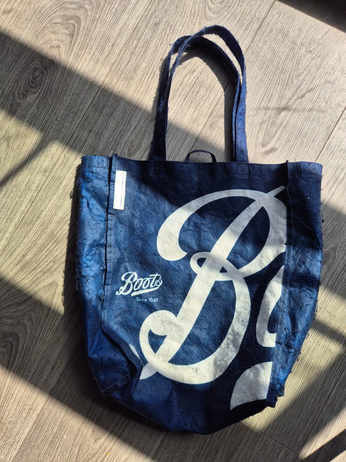 The raggedy bag itself — a faded navy Boots tote, the fabric gone soft, resting on a wooden floor.